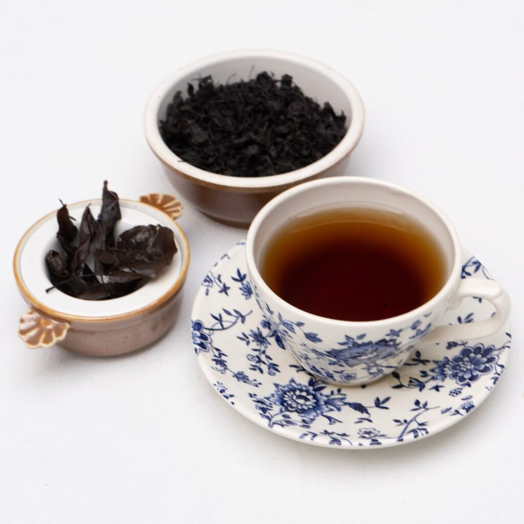 A cup of brewed tea next to a bowl of loose pear leaves on a white background.
