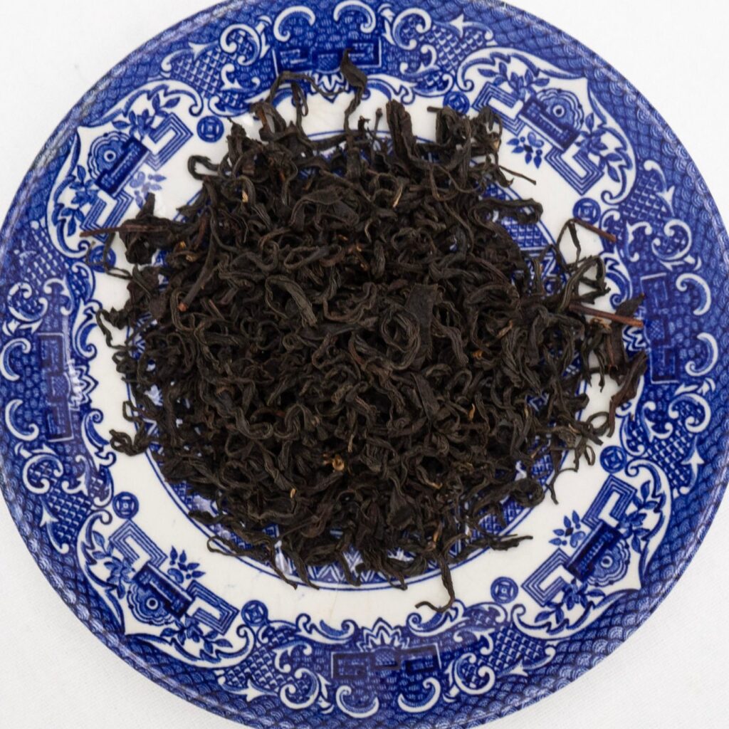 Dried black tea leaves arranged on a blue and white decorative plate.