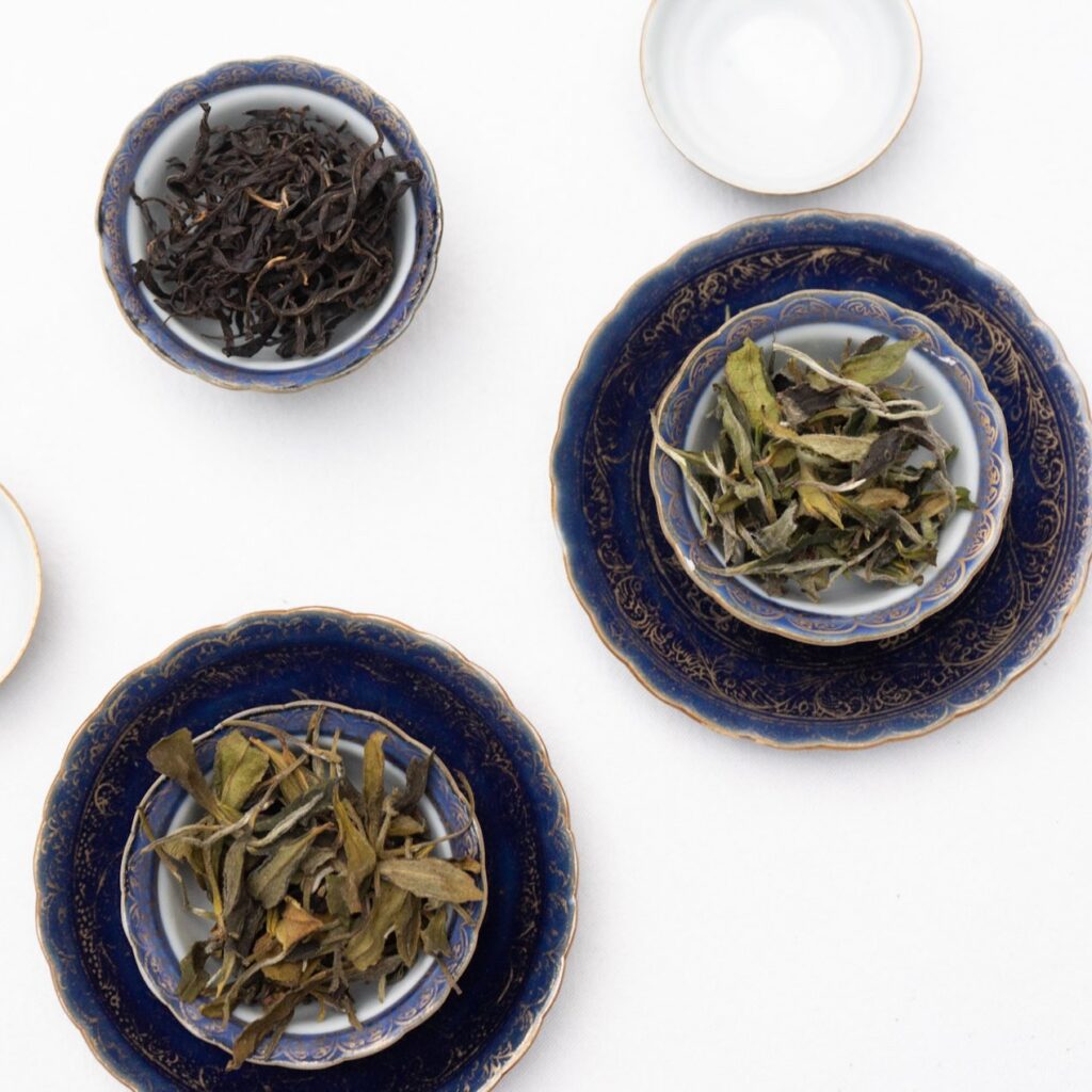 Assorted Tea Leaves in Decorative Bowls Three bowls containing different types of tea leaves arranged on decorative plates.