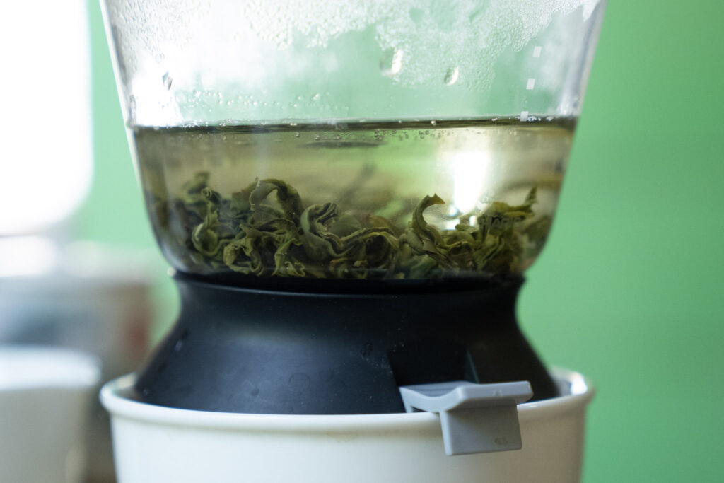 Close-up of a tea infuser containing steeping green tea leaves in hot water.