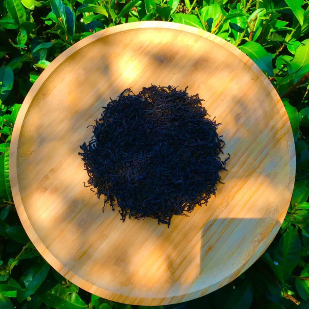 Dried black tea leaves arranged in a circular shape on a wooden plate.