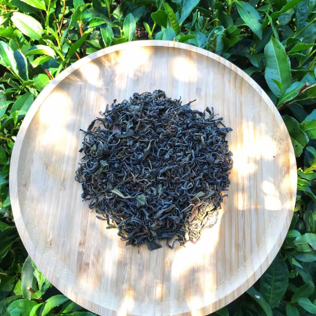Dried green tea leaves arranged in a circular pattern on a wooden tray.