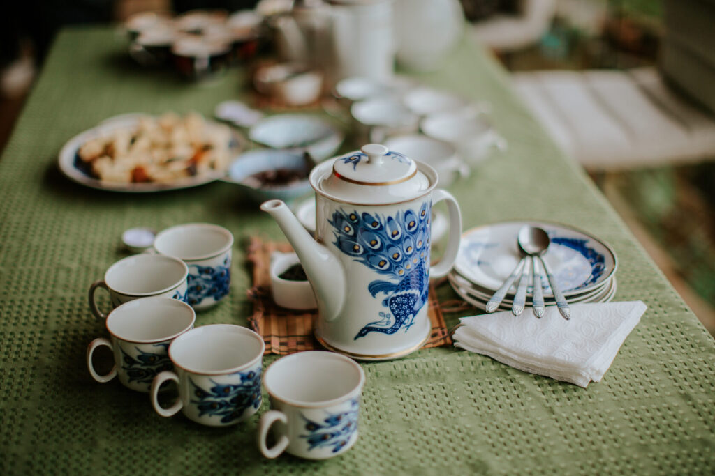 Ceramic teapot with blue peacock design alongside matching cups and saucers on a green tablecloth.