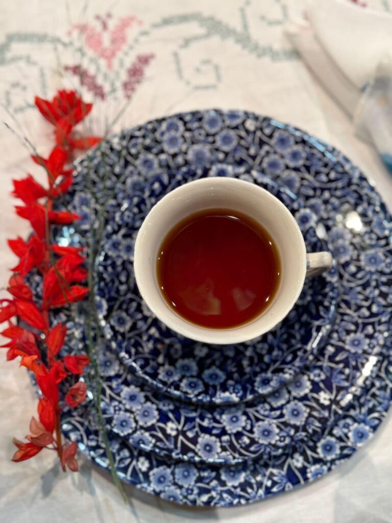 A white cup filled with tea placed on blue decorative plates with red flowers nearby.
