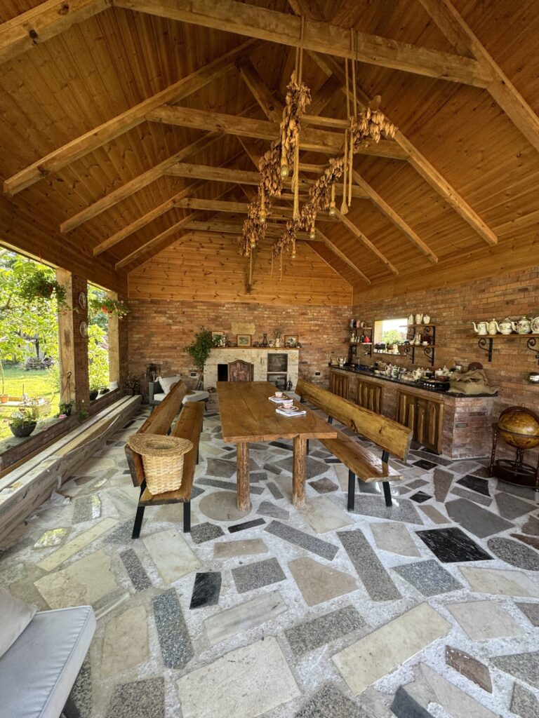 Interior view of a rustic patio featuring a wooden dining table and benches with stone flooring at the Zhgenti plantation