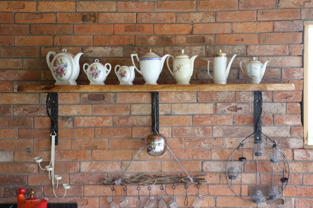 A row of decorative teapots displayed on a wooden shelf against a brick wall.