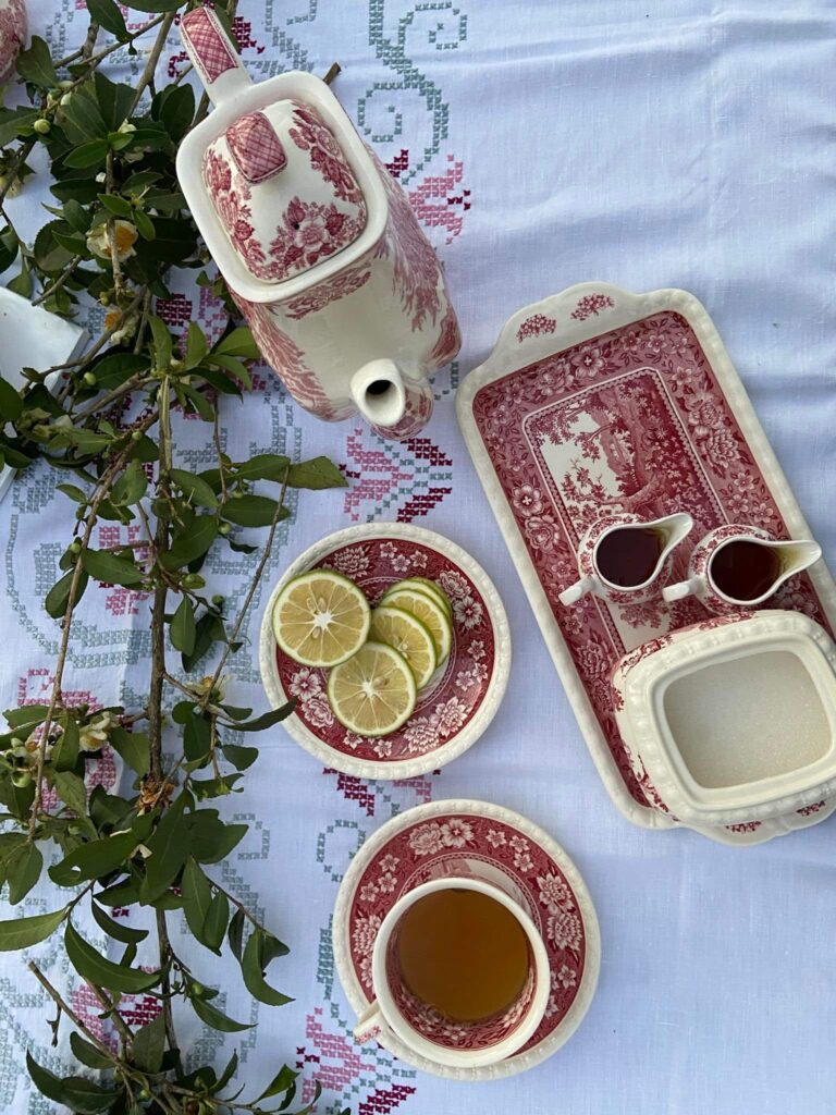 A traditional teapot with matching cups and plates, featuring a floral design, alongside sliced lemons and a small dish.