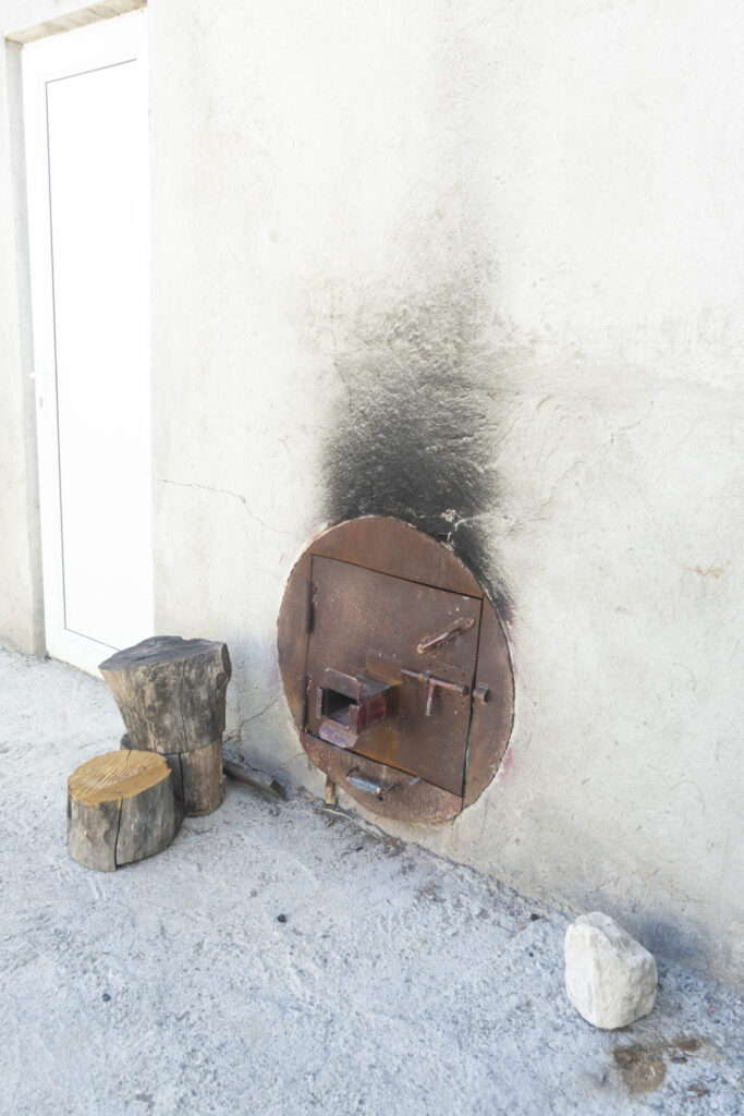Metal stove insert built into a wall with a wooden stool placed nearby.