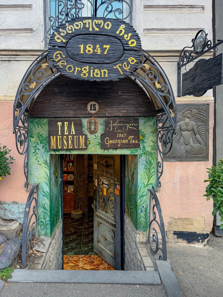 Georgian Tea Museum entrance featuring an arched wooden doorway with gold lettering signage, green mural framing, and the number 1847 above the door